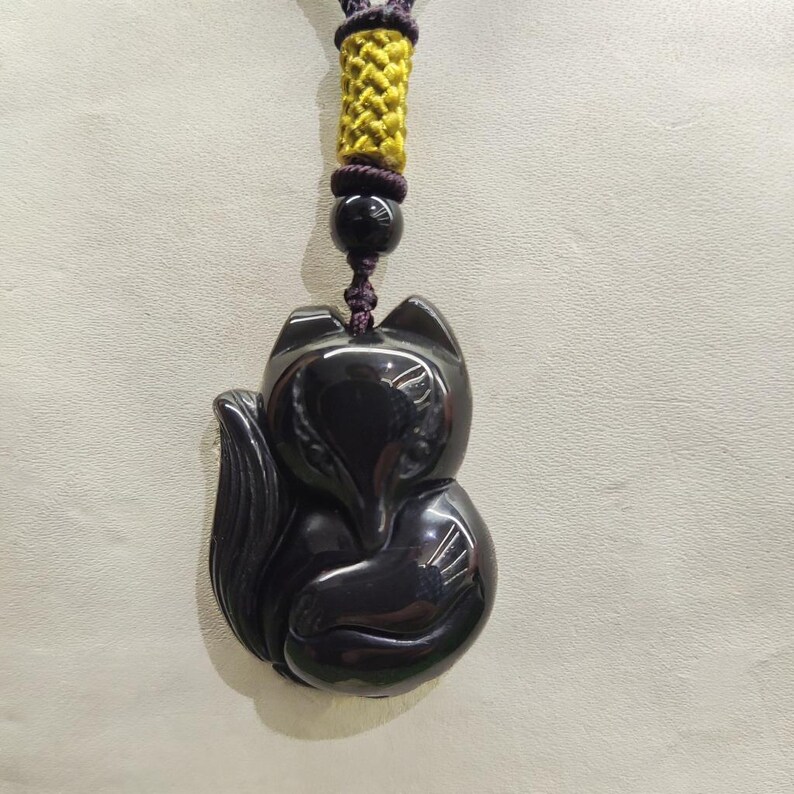 May include: A black fox pendant necklace. The pendant is a glossy, carved fox figure. The necklace cord is purple and yellow, with a black bead. The fox is a stylized, seated design.