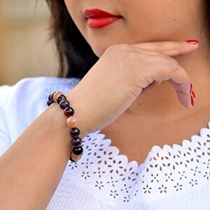 May include: A beaded bracelet featuring a mix of dark brown, purple, and peach-colored stones. The bracelet is worn on a wrist, with the beads strung together to form a circular shape. The bracelet is a piece of jewelry.