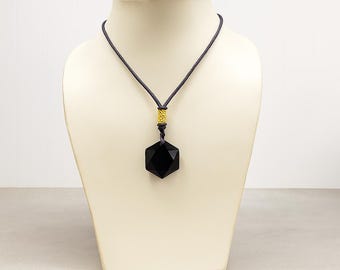 Puede incluir: Collar con colgante geométrico negro. El colgante, de forma facetada, está suspendido de un cordón oscuro. Un elemento dorado se sitúa encima del colgante. Se muestra sobre un maniquí.