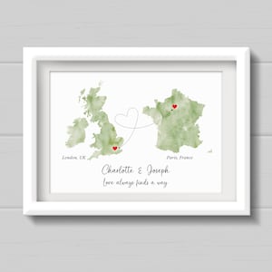May include: A white framed print showing watercolour maps of the UK and France, with red hearts marking London and Paris. The names "Charlotte & Joseph" and the phrase "Love always finds a way" are below the maps. The maps are green.