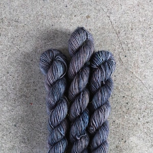 May include: Three skeins of yarn in shades of blue and purple. The yarn is a fingering weight and has a subtle speckled effect.