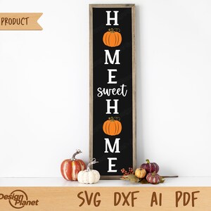 Può includere: Un cartello nero con testo bianco che recita "Home sweet Home" con una grafica di zucca tra ogni lettera. Il cartello è incorniciato in legno e si trova su una superficie bianca con zucche davanti.