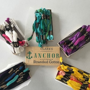 May include: A collection of six boxes of Anchor Fast Colour Stranded Cotton embroidery floss. The boxes are arranged in a circle around a larger box with the Anchor logo and the text "Clark's Anchor Fast Colour Stranded Cotton". The floss is in a variety of colours, including white, pink, purple, blue, green, yellow, and orange.