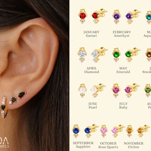 Może przedstawiać: Zestaw 12 złotych kolczyków z różnymi kolorowymi kamieniami szlachetnymi, reprezentujących każdy miesiąc roku. Kamienie szlachetne obejmują granat, ametyst, akwamaryn, diament, szmaragd, kwarc dymny, perłę, rubin, perydot, szafir, różowy kwarc, cytryn i czarny onyks.