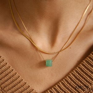 May include: A gold chain necklace with a green square pendant. The necklace is layered with two chains.