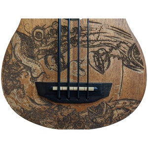 Może przedstawiać: Basowy gitar elektryczny wykonany z drewna z wypalonym na nim szczeg&oacute;łowym, skomplikowanym wzorem. Wz&oacute;r przedstawia serce, rybę i inne abstrakcyjne kształty.
