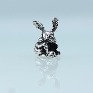 Può includere: Un ciondolo d'argento a forma di coniglio seduto e che tiene una carota nelle zampe.
