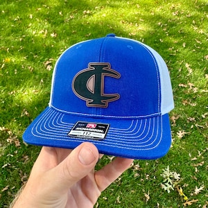 May include: A blue and white trucker hat with a black and copper 'C' logo. The hat is adjustable and has a Richardson 112 label.