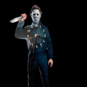 May include: A clock featuring a translucent image of Michael Myers, the iconic horror movie character, holding a knife. The clock face is visible through his body, with the numbers 1 through 12 displayed in white.