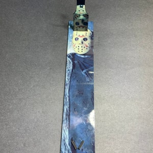 May include: A black metal stand with a silver finish, designed to hold a hockey mask. The stand has a printed image of a hockey mask with a white background and a blue and white pattern.