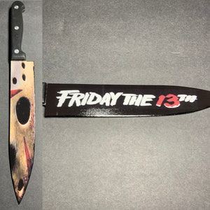 May include: A black and silver knife with a red and white graphic of Jason Voorhees's mask and the text "Friday the 13th".