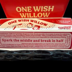 May include: A novelty item featuring a red and white box labeled "ONE WISH WILLOW." The box contains a small, dark-colored, twig-like object. Text on the box reads "Spark the middle and break in half."