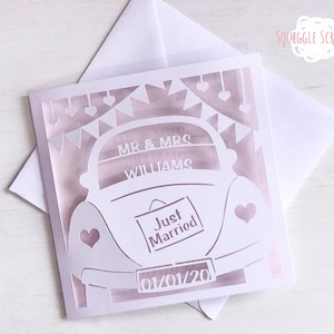K&ouml;nnte beinhalten: Eine wei&szlig;e Karte mit einem ausgeschnittenen Design eines Autos mit den Worten "Just Married" auf der R&uuml;ckseite. Das Auto hat ein Banner dar&uuml;ber, auf dem "Mr. & Mrs. Williams" und das Datum "01/01/20" steht.