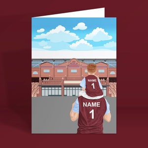 May include: A father and son wearing matching maroon and blue jerseys with the number "1" and the word "NAME" on the back. They are standing in front of a brick building with a blue sky and white clouds in the background.