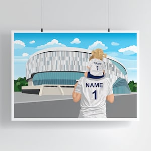 May include: A father and daughter wearing matching white soccer jerseys with the number "1" and the word "NAME" on the back. They are standing in front of a large stadium with a blue sky and white clouds in the background.