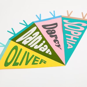 K&ouml;nnte beinhalten: Ein farbenfroher Filz-Wimpelbanner mit den Namen Oliver, Danjan, Darcy und Sophia in einer Retro-Schrift. Die Wimpel sind gelb, gr&uuml;n, rosa und blau.