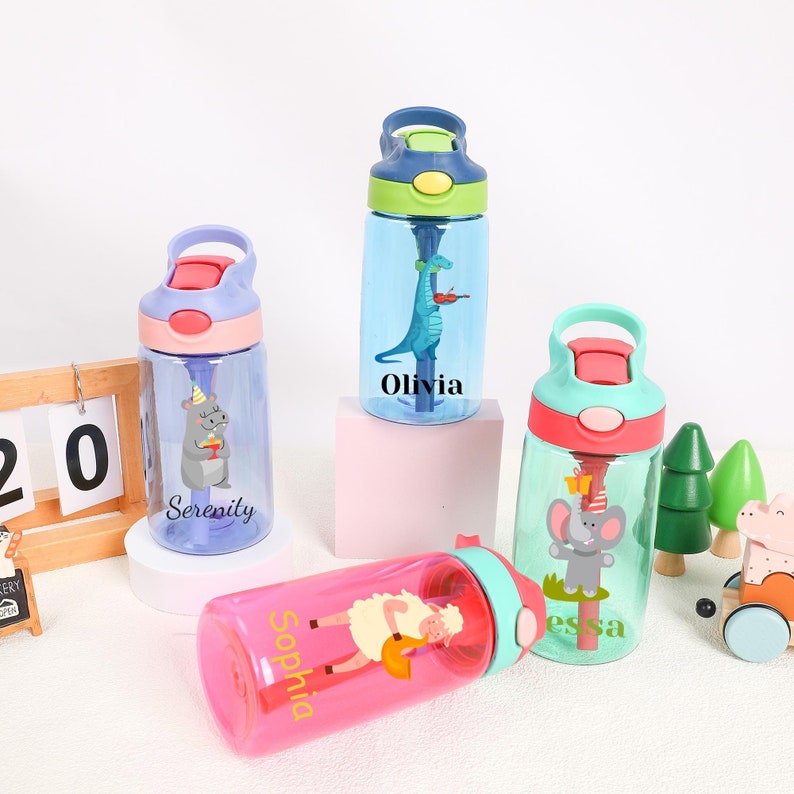 Pu&ograve; includere: Quattro bottiglie d'acqua riutilizzabili colorate con coperchi a cannuccia e nomi personalizzati. Le bottiglie presentano vari disegni di animali, tra cui un dinosauro, un ippopotamo, un elefante e una pecora. Le bottiglie sono su una superficie rosa chiaro, blu chiaro e bianca.