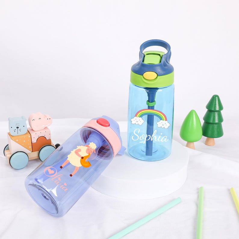Pu&ograve; includere: Due borracce personalizzate blu e viola con tappi a cannuccia. Una borraccia ha un design arcobaleno e nuvole con il nome "Sophia" su di essa. L'altra borraccia ha un design di pecora dei cartoni animati con il nome "Mila" su di essa.