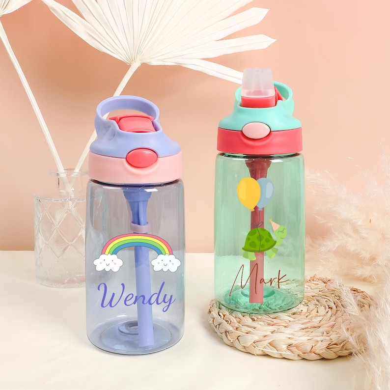 Pu&ograve; includere: Due bottiglie d'acqua in plastica trasparente con disegni colorati e i nomi "Wendy" e "Mark" su di esse. Le bottiglie hanno una cannuccia e un tappo a levetta.
