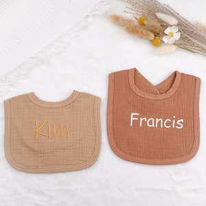 May include: Two brown muslin bibs with white embroidery. The bib on the left says "Kim" and the bib on the right says "Francis".