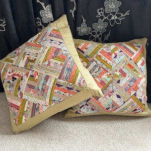 May include: Two decorative pillows with a geometric pattern of colorful fabric strips. The pillows have a beige border and are made of a soft, textured fabric.
