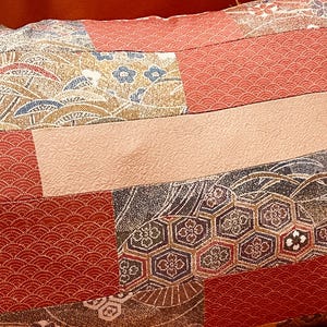 Könnte beinhalten: Nahaufnahme eines Patchwork-Textils mit einer Vielzahl von Mustern und Farben. Das Design umfasst rote, beige und marineblaue Abschnitte mit floralen, geometrischen und wellenartigen Motiven. Der Stoff scheint gesteppt zu sein.