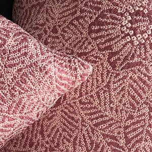 Könnte beinhalten: Nahaufnahme von zwei dekorativen Kissen und einem Stoff mit sich wiederholendem Muster. Die Kissen und der Stoff sind in einem tiefen Rosaton gehalten und haben ein weißes, geometrisches Design. Das Muster besteht aus kleinen, verbundenen Formen.