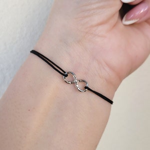 Può includere: Un braccialetto in corda nero con un ciondolo infinito in argento. Il ciondolo ha una superficie testurizzata.