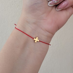 Puede incluir: Un brazalete de cuerda roja con un pequeño dije de cruz dorada.
