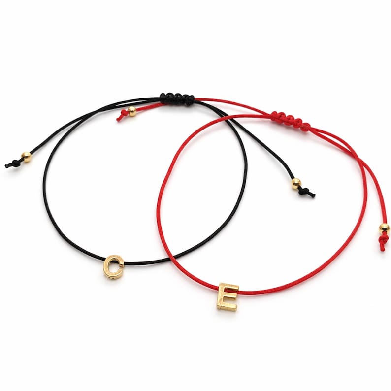 May include: Two adjustable string bracelets. One is black with a gold-colored letter "C", the other is red with a gold-colored letter "E". Both bracelets have gold-colored beads and adjustable knots.