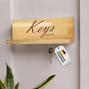 May include: Wooden key holder with the word "Keys" in a script font. The key holder has a small shelf and a set of keys hanging from it. A tag that says "Handmade in Germany" is attached.