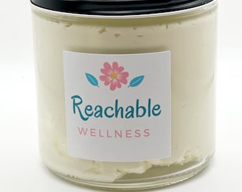 May include: A glass jar filled with a white cream product. The jar has a black lid and a white label with a pink flower and the text "Reachable Wellness".