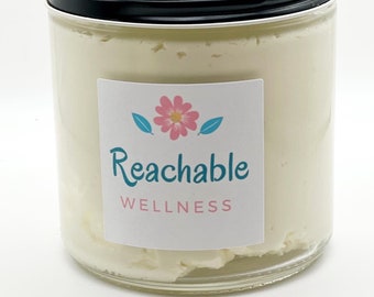 May include: A glass jar filled with a white cream product. The jar has a black lid and a white label with a pink flower and the text "Reachable Wellness".