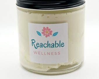 May include: A glass jar with a black lid filled with white cream. The jar has a label that says "Reachable Wellness" with a pink flower and green leaves.