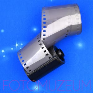 以下が含まれることがあります： 青い背景に、部分的に巻き戻された35mmフィルムのロール。フィルムはグレーで、端にスプロケット穴があります。フィルムカートリッジは黒です。「FOTOMUZEUM」の文字がピンク色で見えます。