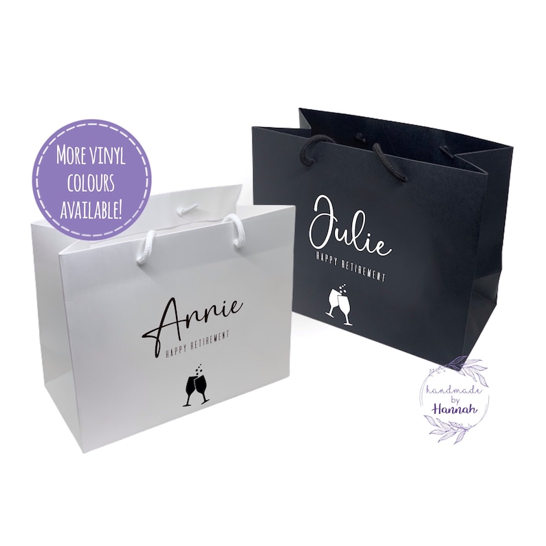 Peut inclure: Deux sacs cadeaux blancs avec des poign&eacute;es noires et du texte noir. Les sacs sont personnalis&eacute;s avec les noms "Annie" et "Julie" et le texte "Joyeux Retraite". Chaque sac a un graphique de deux verres de champagne avec des bulles. Les sacs sont sur un fond blanc.