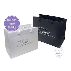 May include: Two gift bags, one white and one black, with the text "Happy Golden Wedding Anniversary" and "Happy Silver Wedding Anniversary" printed on them. The bags are made of paper and have white handles.