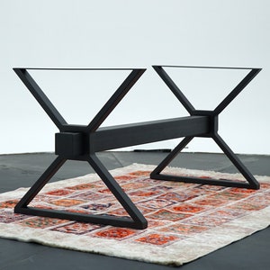 May include: Black metal table base with a rectangular crossbar and a geometric X-shaped design. The base is sitting on a patterned rug.