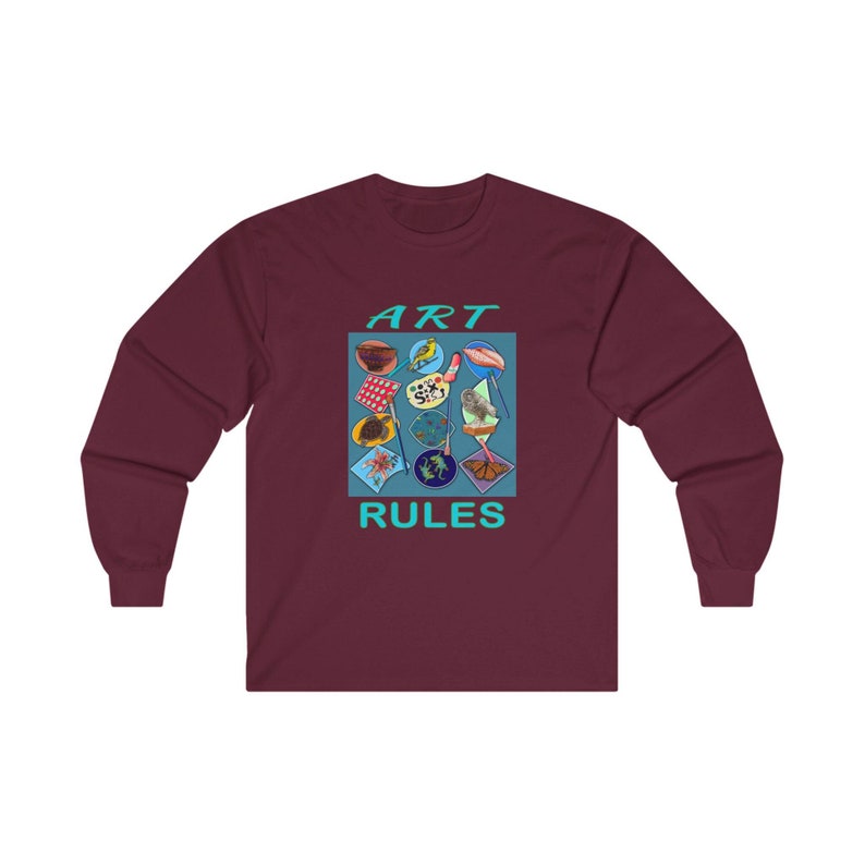 Pu&ograve; includere: Una t-shirt a maniche lunghe color granata con un design grafico di un quadrato blu che contiene varie immagini colorate. Il testo "ART RULES" &egrave; stampato in turchese sotto il quadrato.
