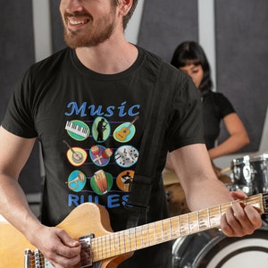 Pode incluir: Uma pessoa vestindo uma camiseta preta com o texto "Music Rules" e um gráfico de instrumentos musicais. A pessoa está tocando uma guitarra elétrica marrom.