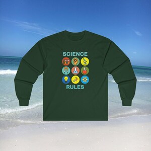 Op de afbeelding: Een donkergroen longsleeve t-shirt met de tekst "SCIENCE RULES" in blauw en wit. Het shirt heeft een afbeelding van negen kleurrijke wetenschappelijke iconen.
