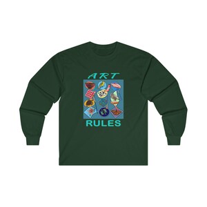 Pu&ograve; includere: Una maglietta a maniche lunghe verde scuro con una grafica quadrata blu che dice "ART RULES" in testo turchese. La grafica presenta una variet&agrave; di immagini colorate, tra cui una tavolozza di colori, un uccello e una farfalla.