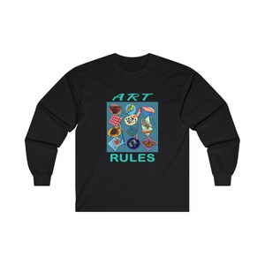 Pu&ograve; includere: Maglietta a maniche lunghe nera con un design grafico di materiali artistici colorati e il testo "ART RULES" in turchese.