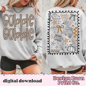 May include: A light gray sweatshirt with the words "Gobble Gobble" in a checkered pattern on the front. The back features Thanksgiving-themed graphics, including a turkey, pumpkin, and the phrase "Gobble Til You Wobble."