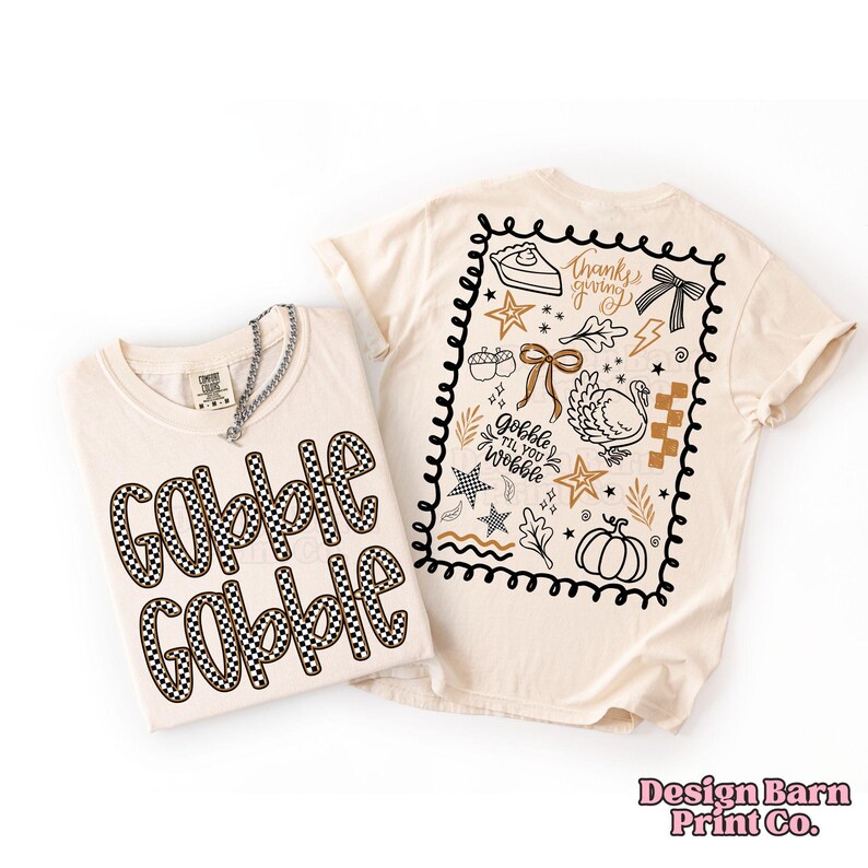 May include: Two cream-colored t-shirts. One shirt has "Gobble Gobble" in a black and white checkered pattern. The other shirt has a black border with Thanksgiving-themed graphics and the text "Gobble Til You Wobble".
