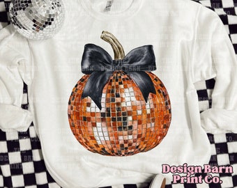 May include: A white sweatshirt with a black bow and a pumpkin-shaped disco ball design. The pumpkin is orange and gold with a black bow.