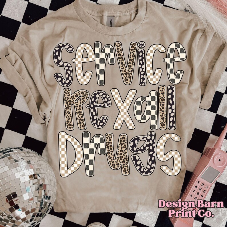 May include: Beige t-shirt with the words "SERVICE REXALL DRUGS" in a mix of leopard print, checkered, and solid black and white lettering. The shirt has short sleeves and a crew neck. The Design Barn Print Co. logo is in the bottom right corner.