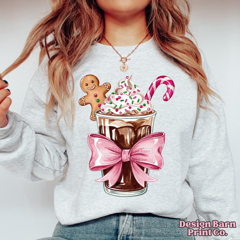K&ouml;nnte beinhalten: Ein graues Sweatshirt mit einem festlichen Design, das einen Lebkuchenmann, ein Schokoladengetr&auml;nk mit Schlagsahne und Streuseln sowie einen Zuckerstock zeigt.
