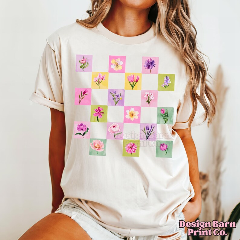May include: Cream-colored t-shirt featuring a grid of colorful watercolor flowers in pink, yellow, purple, and green squares. The shirt has short sleeves and a crew neck. The text "Design Barn Print Co." is visible at the bottom right.