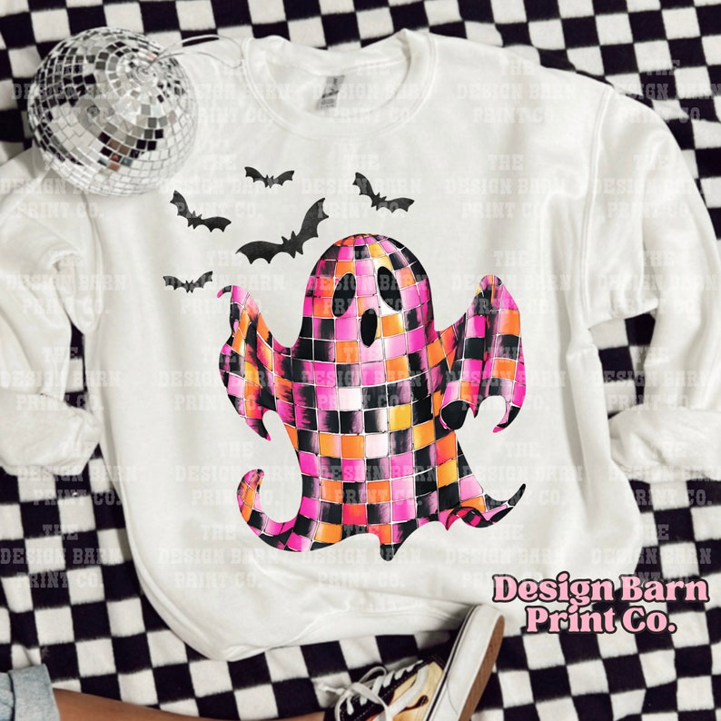 May include: White sweatshirt with a pink, orange, and black checkered ghost design. The ghost has a black outline and a black mouth. There are black bats flying around the ghost. The text "Design Barn Print Co." is printed in pink on the bottom right corner of the sweatshirt.